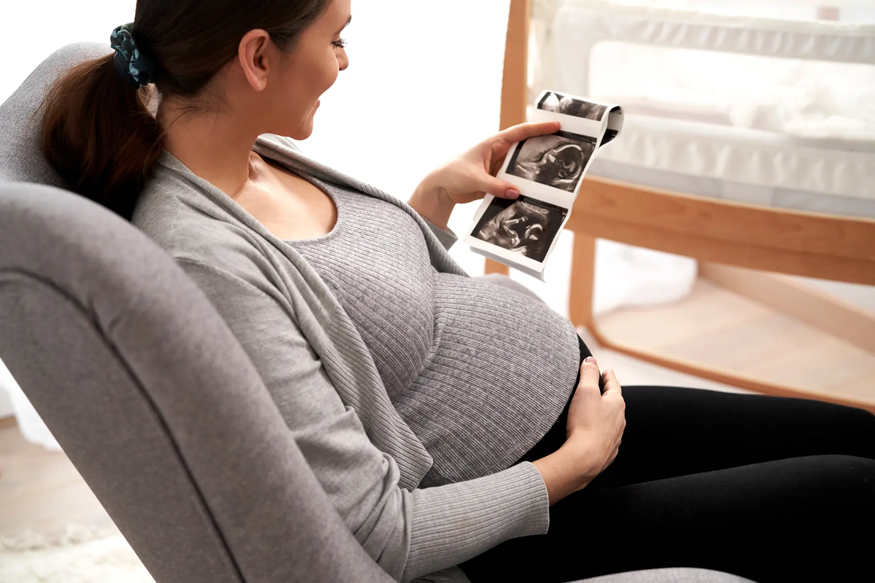 Caucasian woman in advanced pregnancy browsing ultrasound scan in baby's room